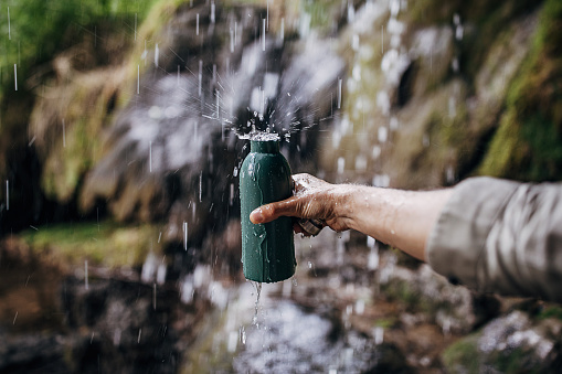 Young man hiker refills his stainless steel bottle with clean and fresh water.