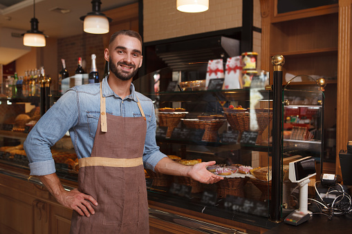 Cheerful male baker welcoming you at his bakery store, copy space