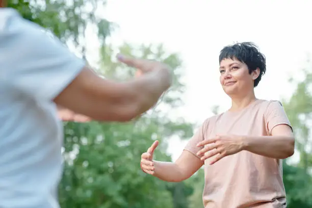 Content attractive brunette coach moving arms with student while developing imagination at qigong practice