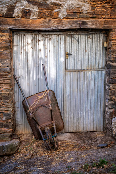 vecchia carriola arrugginito sostenuta da una porta di metallo, scena rurale - vehicle door rusty old fashioned old foto e immagini stock