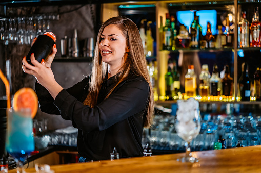 Beautiful female bartender making cocktails on bar counter.
