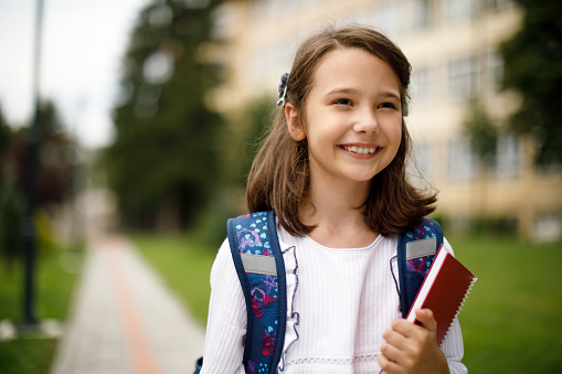 Portrait of cute smiling schoolgirl in front of the school