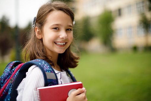 Portrait of cute schoolgirl in front of the school