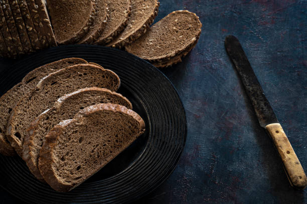 Wholegrain bread slices in a row on dark gray rustic background with vintage bread knife