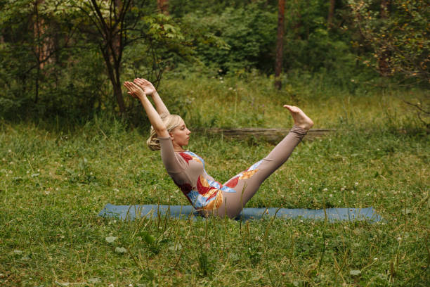 istock Young yogi woman practicing yoga, doing Paripurna Navasana exercise, boat pose, working out, wearing sportswear, on fitness mat in the Park around pine trees. 1269933090