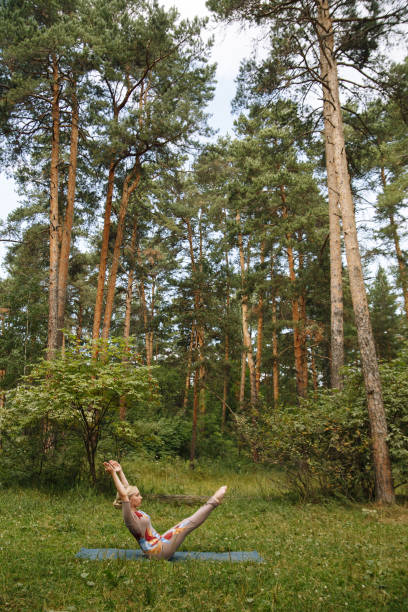 istock Young yogi woman practicing yoga, doing Paripurna Navasana exercise, boat pose, working out, wearing sportswear, on fitness mat in the Park around pine trees. 1269933145