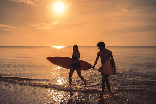 Young asian couple holding surfboard on the beach at morning
