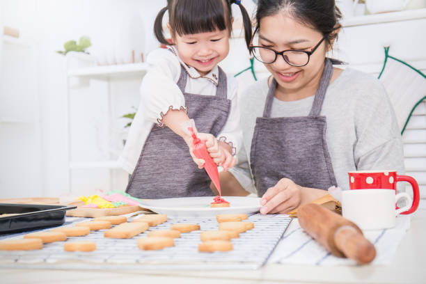 小さなアジアの女の子と彼女の母親が台所でケーキとクッキーを焼く肖像画。幸せなアジアの家族と母の日の概念 - bread bakery women cake ストックフォトと画像
