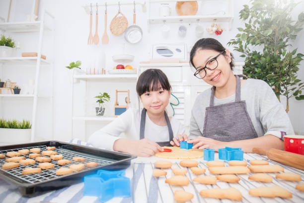 小さなアジアの女の子と彼女の母親が台所�でケーキとクッキーを焼く肖像画。幸せなアジアの家族と母の日の概念 - bread bakery women cake ストックフォトと画像