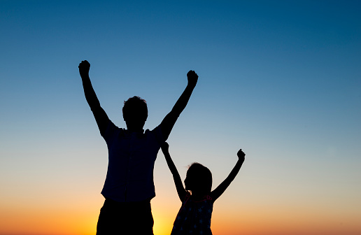 Father and her daughter are raising arms, silhouette.