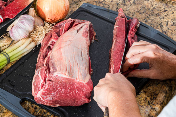 Chef cutting a fresh piece of beef tenderloin over the sink.