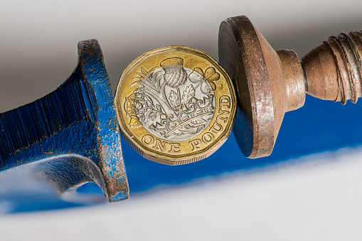 Concept for financial stress or recession with UK one pound sterling coin being squeezed between the jaws of a large vise. Detailed macro shot of vice