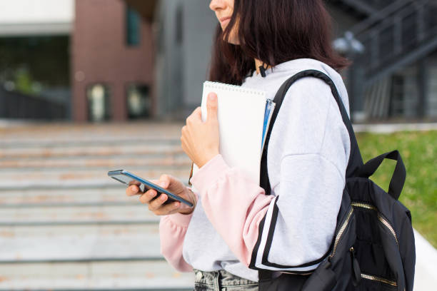 istock A female student with a black backpack holds a smartphone and Notepad on the threshold of the University. Higher education, the beginning of the school year, return to school, gadgets. Copyspace 1269938698