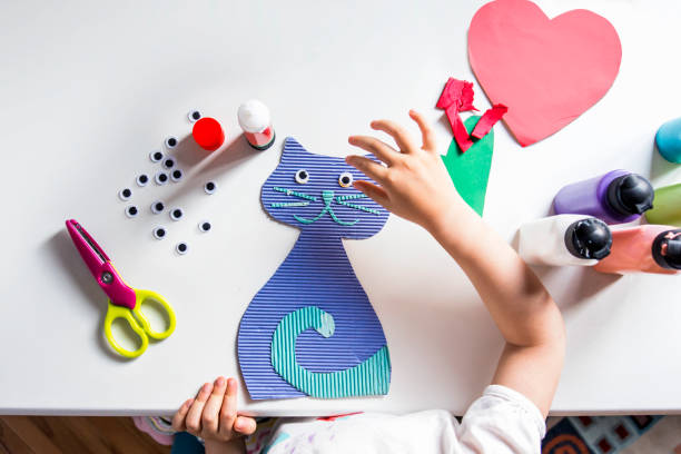 Little girl sticks googly eyes on a handcrafted cat figure stock photo
