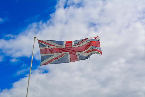 A British union jack flag blowing in the wind with a blue sky and cloud background