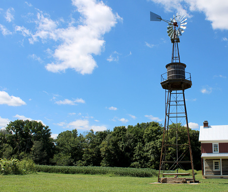Farm windmill on a beautiful day with bright blue sky and white clouds in Ohio - trees and a house below