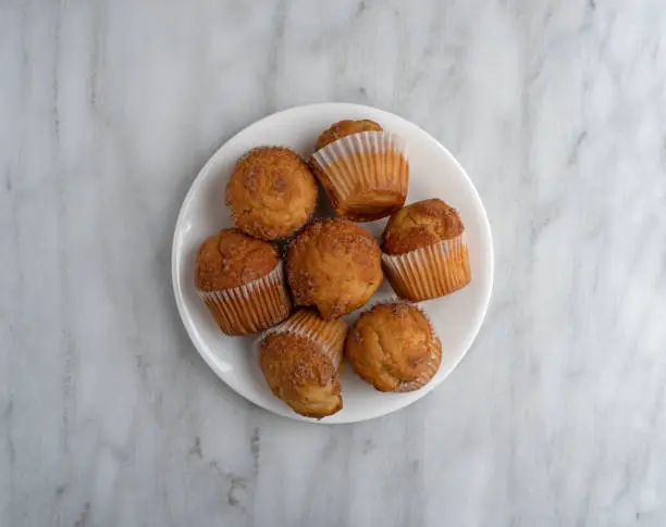 Top view of several banana Streusel muffins on a white plate atop a marble tabletop.