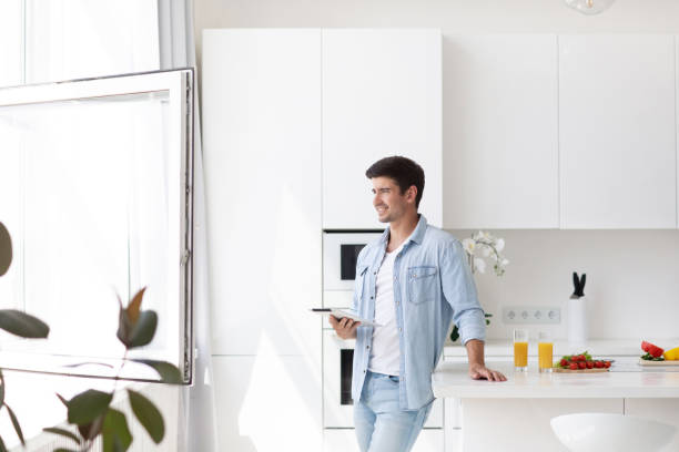 istock Young man standing on domestic kitchen holds digital tablet searching recipes for cook vegetable salad healthy food. 1269948516