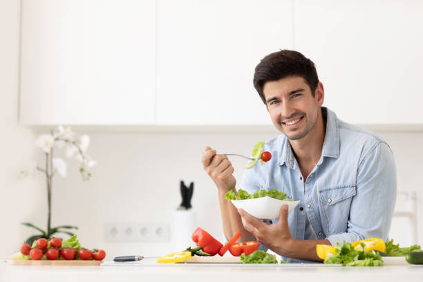 istock Handsome man eating salad with fresh vegetables in the kitchen. 1269948605