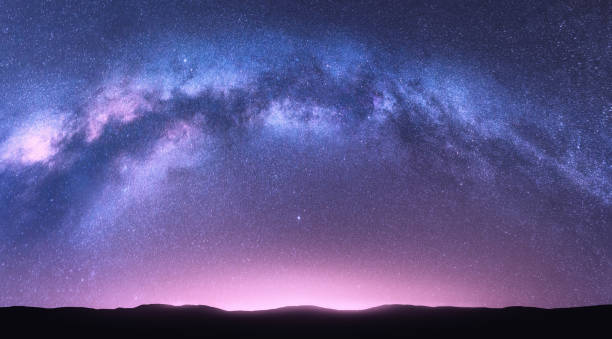 天の川アーチ。明るいアーチ型の天の川、星、ピンクの光と丘と紫の空と幻想的な夜の風景。宇宙と美しいシーン。星空のあるスペースの背景。銀河と自然 - 天の川 写真 ストックフォトと画像