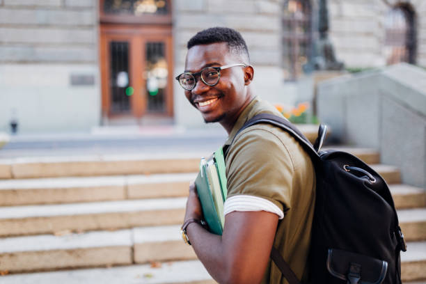 Portrait of a young African American male student going to a university Young African American male student sitting on a staircase university student stock pictures, royalty-free photos & images