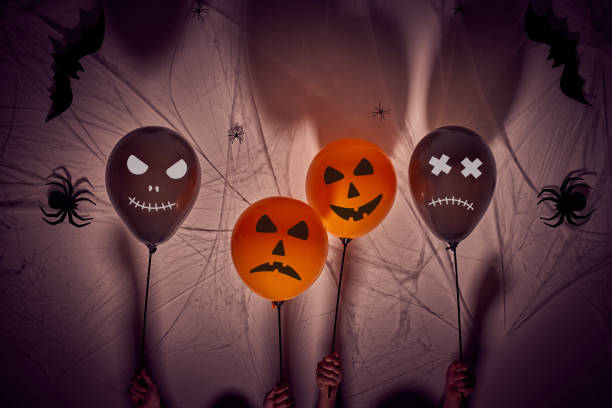 istock Halloween balloons with horror faces held by 7 year old children's hands. Dark background with shadows, spiders, spiderwebs and bats. 1269956083