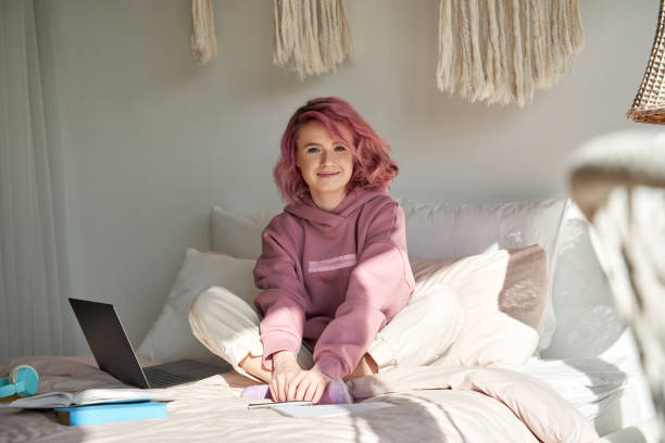 feliz hipster adolescente con el pelo rosa sentarse en la cama estudio en línea mirar a la cámara - twenty first fotografías e imágenes de stock