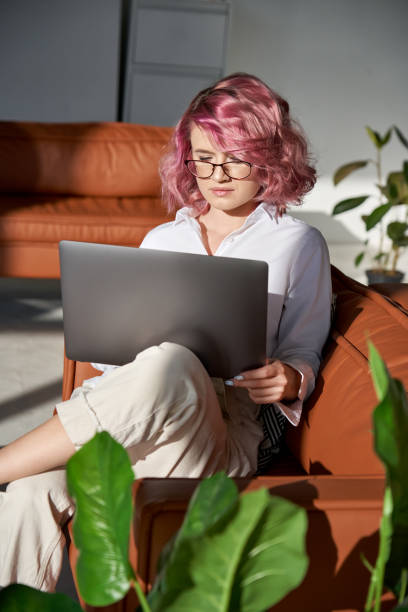 молодая женщина, используя портативный компьютер дома онлайн сидя на диване, вертикальной. - gen z стоковые фото и изображения