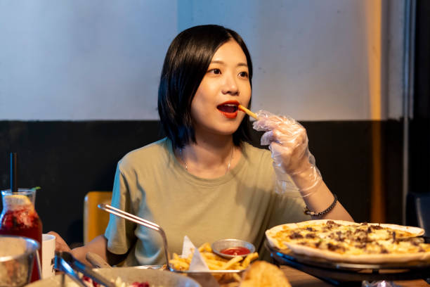 A beautiful Asian woman eating French fries with plastic gloves In Guangzhou. chinese ethnicity china restaurant eating stock pictures, royalty-free photos & images