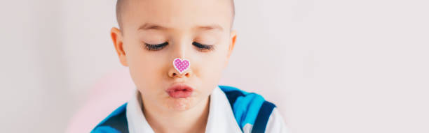 Cross-eyed kid looking at purple violet heart sticker on nose. Funny hilarious white Caucasian cute adorable child boy making faces. Valentine Day holiday concept. Web banner header for website. niño de ojos cruzados mirando pegatina de corazón violeta púrpura en su nariz. divertido hilarante blanco caucásico lindo niño adorable haciendo caras. concepto de vacaciones del día de san valentín. encabezado de banner web para el sitio web.
