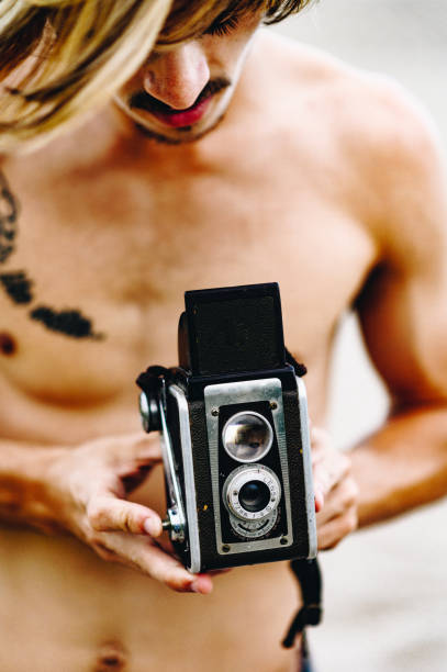 istock Shirtless man uses vintage camera on the beach 1269980972