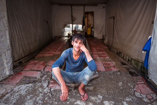 Baku / Azerbaijan - June 7, 2019: portrait of young handsome man sitting in the ground waiting for job in garage shop