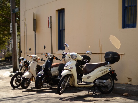 A row for four mopeds/ scooters in cream and black on a suburban street in Sydney Australia