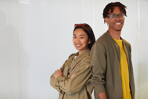 Portrait of multiethnic young couple standing back to back and smiling at camera against the white background