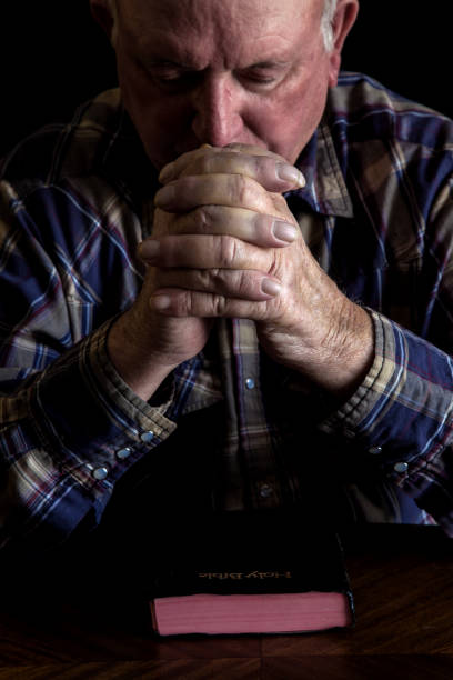 istock Senior man praying with a Bible on a table 1269989988