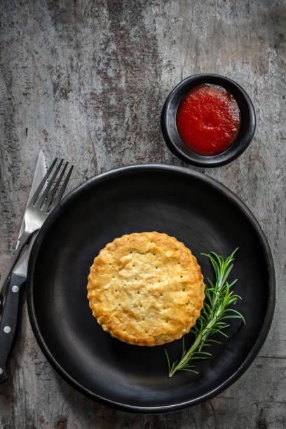 fleischkuchen auf schwarzem teller über rustikalem holz.  mit rosmarin und tomatenuntertasse oder ketchup. - beef pie stock-fotos und bilder