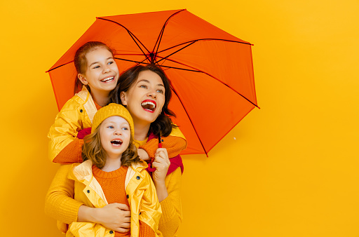 Happy emotional children and their mother laughing and hugging. Family with red umbrella on colored yellow background.