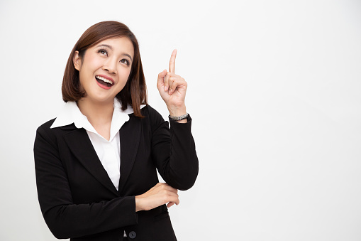 Smiling asian business woman pointing up isolated over white background