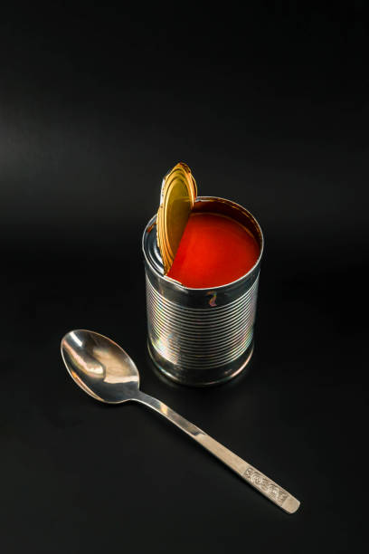 Delicious tomato soup in an open metal can with a spoon on a black background