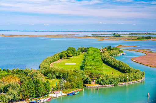 Aerial view of Torcello islands swamp, water canal and green trees alley and bushes. Panoramic view of Venetian Lagoon from bell tower. Veneto Region, Northern Italy. Blue cloudy sky background.