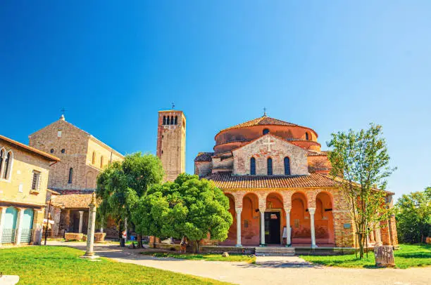 Church of Santa Fosca building on Torcello island, Cathedral of Santa Maria Assunta with bell tower campanile, blue clear sky background. Venetian Lagoon, Veneto Region, Northern Italy.