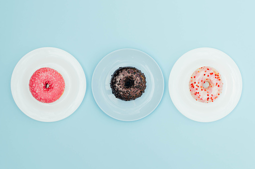 Different bright donuts on a plate on a blue background. Sweet and delicious food.