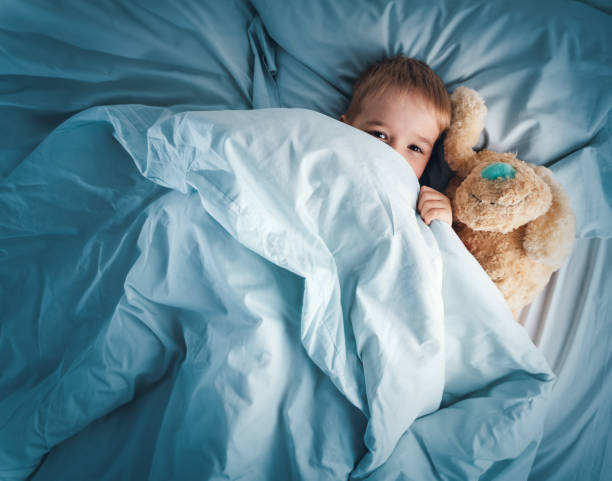 istock Sleepy boy lying in bed with white beddings 1270025297