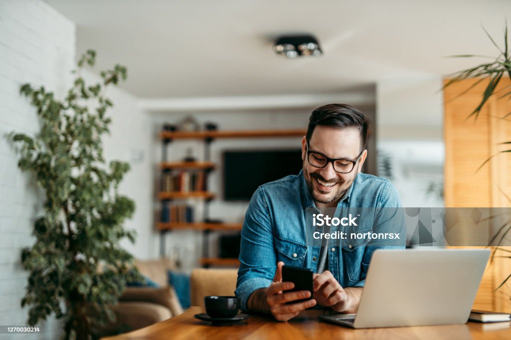 Portrait of a cheerful man using smart phone at home office. Men Stock Photo