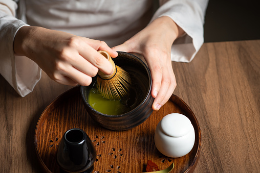 Woman whisking matcha powder while making matcha green tea drink with traditional Japanese accessories for tea ceremony