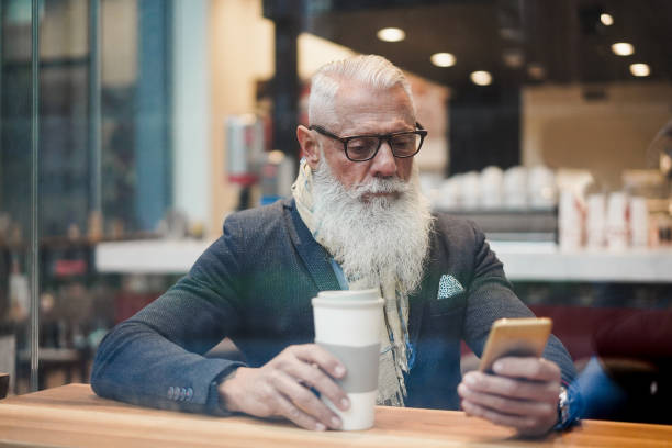 istock Senior business man using smartphone app while drinking coffee inside cafe bar - Trendy entrepreneur doing breakfast - Job, morning break and tech concept - Window from outside view - Focus on face 1270034336