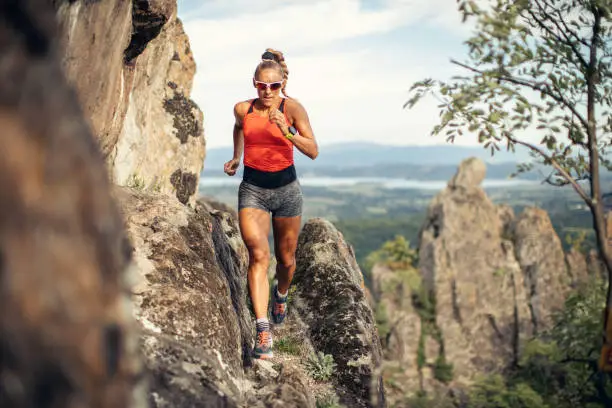 Action photo of extreme sport athlete woman trail runner while running and climbing mountain cliff during her training. Extreme terrain.