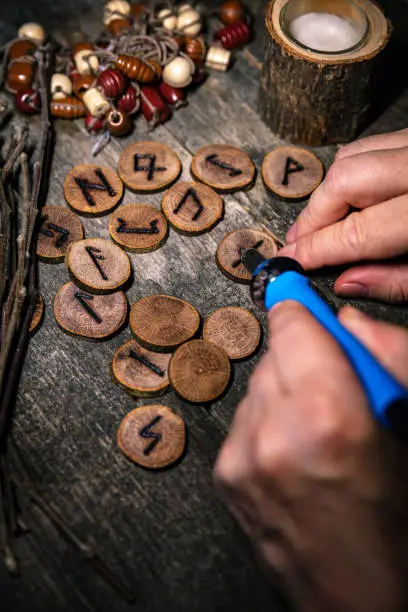 man writing wooden runes with an pyrography or pokerwork, esoteric background, details