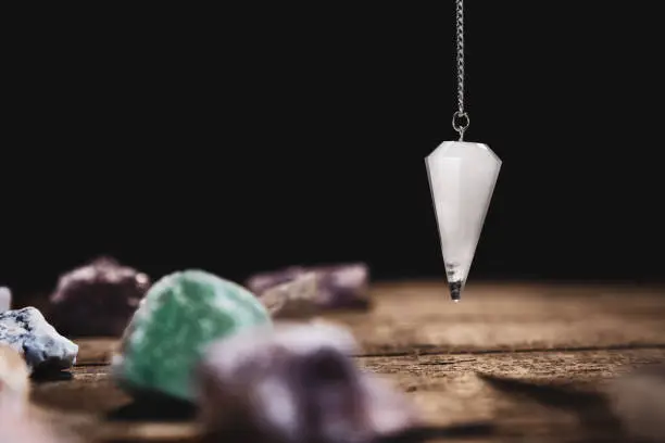 Fortunetelling and horoscope with a pendulum and healing gemstones, black background with copyspace
