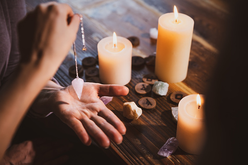 Libra con un péndulo sobre la mano, curación u oráculo de predicción, velas, runas y piedras curativas photo